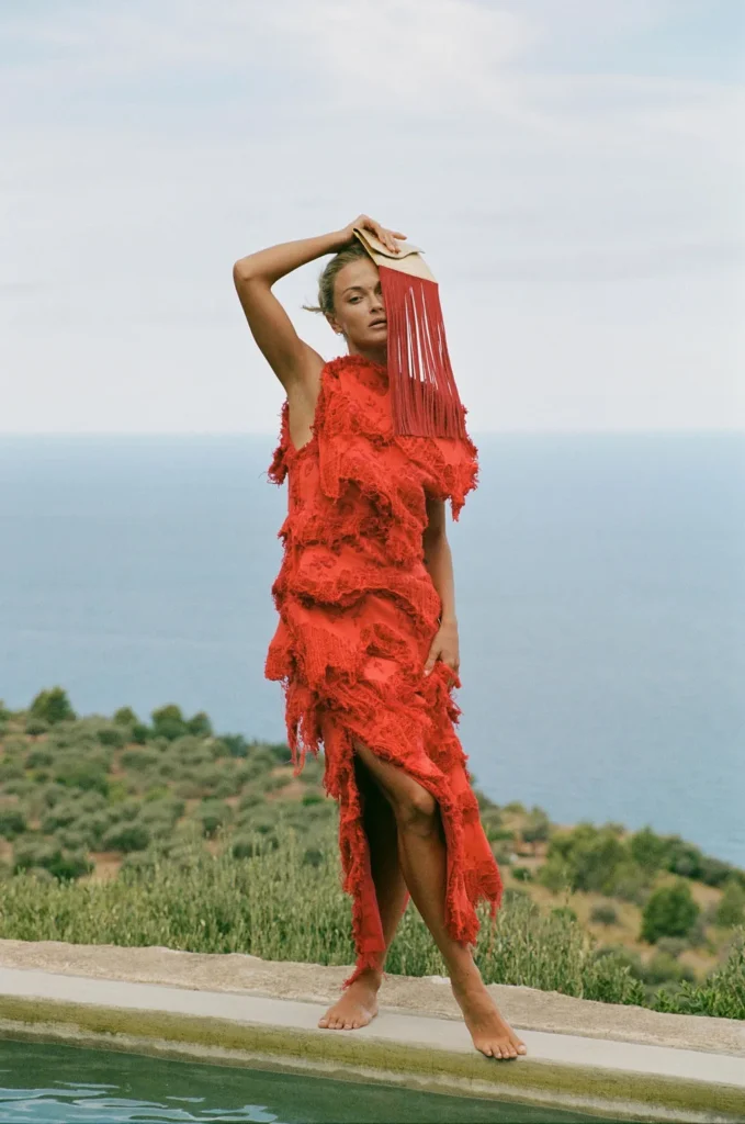 Model holding the Golden Sun gold and red fringe clutch outdoors
