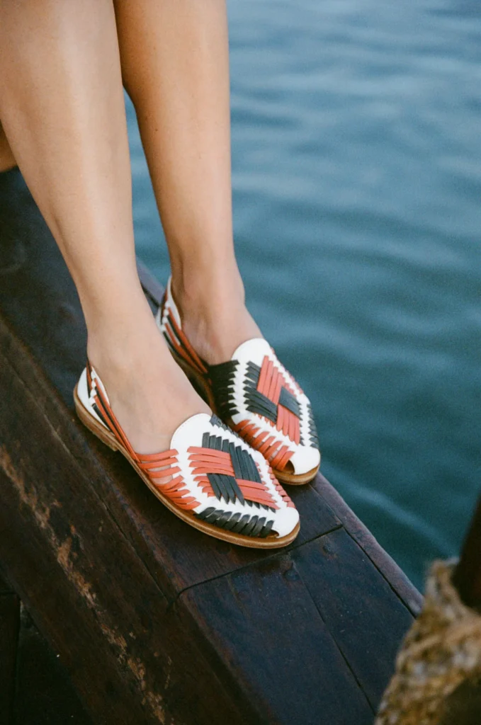 Yuma woven leather espadrilles worn barefoot on a wooden dock beside calm blue water